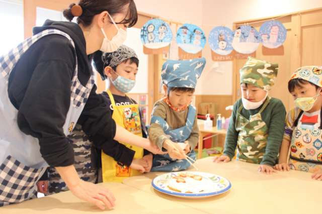 先生と園児たちがクリスマスのホールケーキを作っている写真
