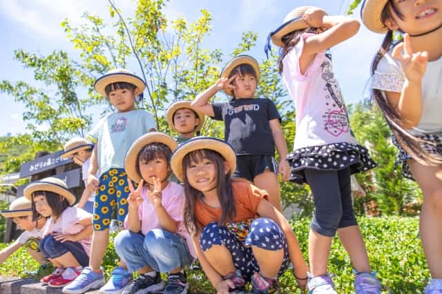 帽子を被った園児達が園庭でカメラ目線でピースをしている写真
