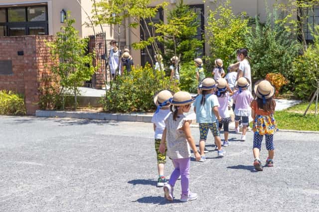 園児達が先生に引率されて一列に並んで門から園舎の中に帰っていく写真