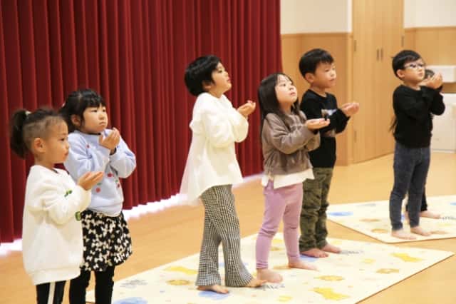 園児達が手を水を救うような形にして少し上を向いている写真