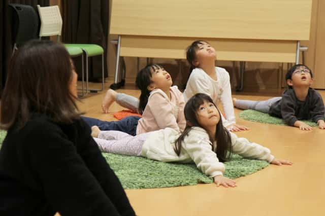 園児達がうつ伏せになり両腕を床につけて体を逸らせ上を向いている写真