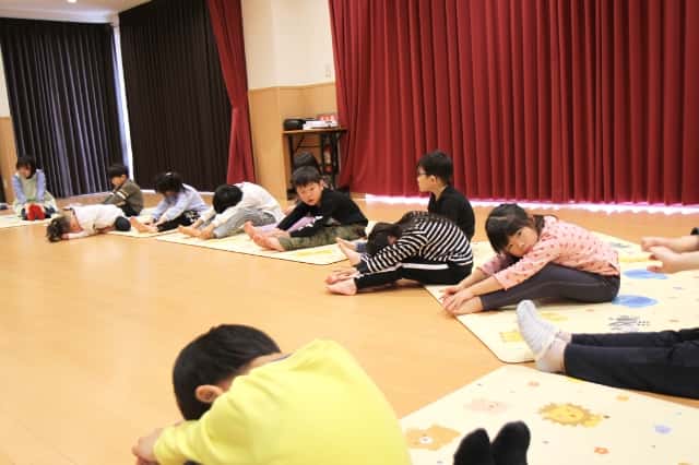 園児達が両足を前に伸ばし前屈をしている写真