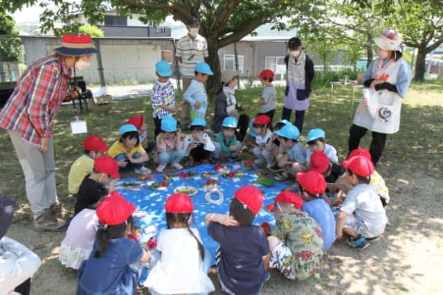 園児達がブルーシートの上で花を使った工作の準備をしている写真