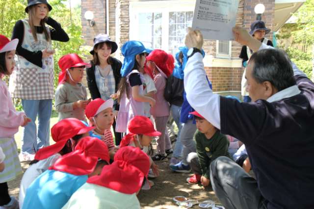 園児達が地面に座って先生の話を真剣に聞いている写真