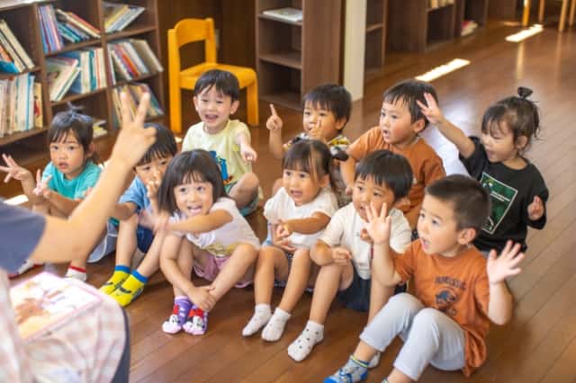 園児達が床に座って先生と同じ手のポーズをしている写真