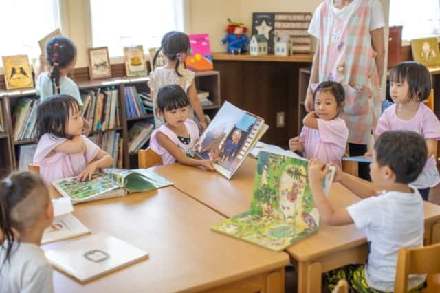 女の子が他の園児達に絵本を見せて何かを話している写真
