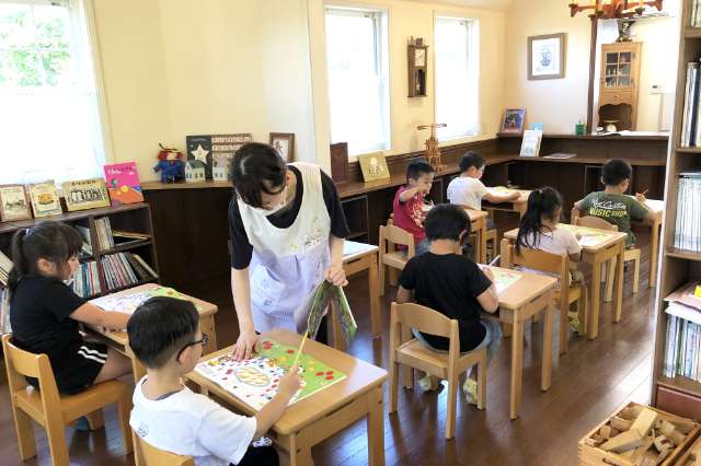 机に向かってワークをしている園児達に先生が教えている写真